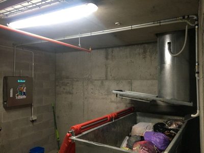Garbage Doctor 3000 on a concrete wall beside a round chute, over a galvanised bin of bagged rubbish