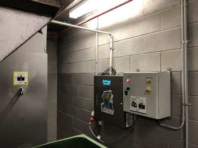 Garbage Doctor 3000 beside its control box on a block wall, above a green waste bin