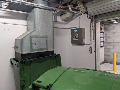 Garbage Doctor 3000 beside a chute discharge over a green 660-litre bin, by the roller door