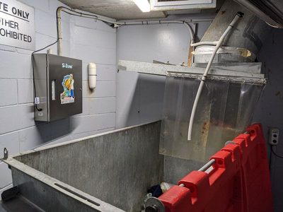 Garbage Doctor 3000 beside the chute's discharge and its strip curtain, over a galvanised waste bin
