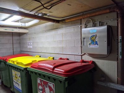 Garbage Doctor 3000 above red- and yellow-lidded recycling and rubbish bins in a garbage room