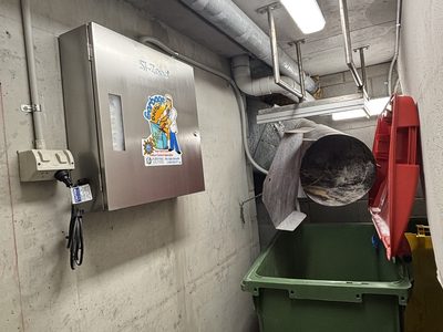 Garbage Doctor 3000 on a narrow bin room wall, beside the chute's discharge over a green rubbish bin