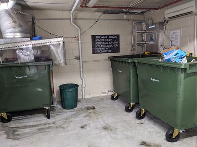 Garbage Doctor 5000 in a garbage room with a bin wash-down area, above green 660-litre bins