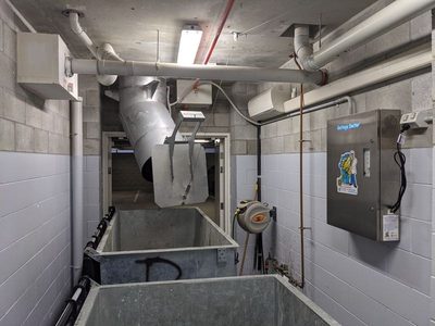 Garbage Doctor 5000 in a narrow garbage room, two galvanised bins under the chute and a hose reel