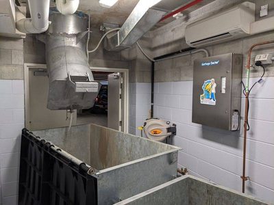 Garbage Doctor 5000 beside a chute discharge over two galvanised refuse bins, with a hose reel