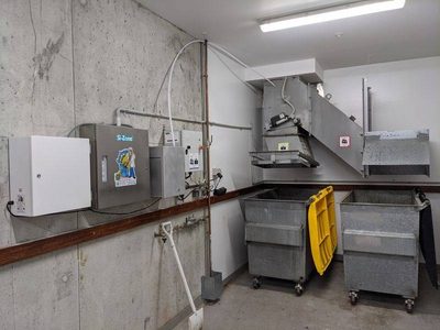 Garbage Doctor Scenting's white cabinets beside a Si-Zone ozone unit, in a bin room with galvanised waste bins
