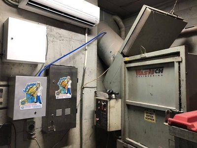 Garbage Doctor Scenting beside a WasteTech garbage compactor, its blue hose to the scent tank