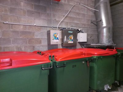 Garbage Doctor Duo beside a galvanised refuse chute, above a row of red-lidded rubbish bins