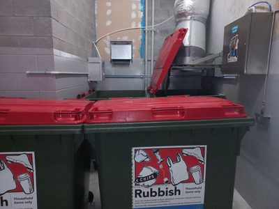 Garbage Doctor Duo above red-lidded bins for household rubbish, beside the chute