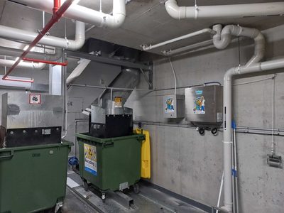 Garbage Doctor Duo and its scent tank beside a chute's discharge, over green waste and recycling bins