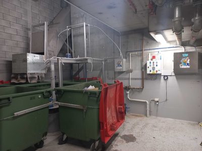 Garbage Doctor Duo in a waste room, a wider view of the garbage chute's discharge over green 660-litre bins