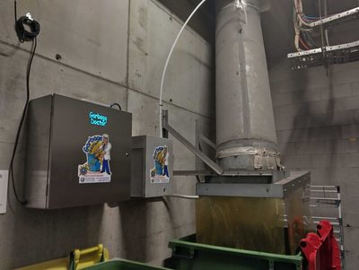 Garbage Doctor Duo and its scent tank beside a galvanised refuse chute, the tank's white pipe into the chute