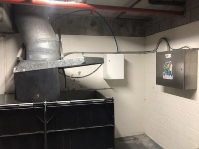Garbage Doctor Duo and its white scent tank beside a galvanised chute over a black-lidded waste bin
