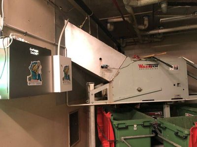 Garbage Doctor Duo and its scent tank beside a WasteTech chute discharge over green waste bins