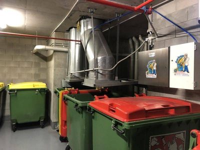 Garbage Doctor Duo and its scent tank beside two garbage chutes over bins with red and yellow lids