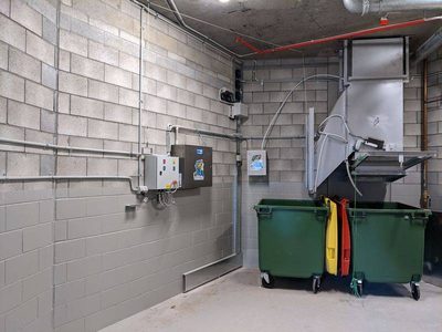Garbage Doctor Duo on a block wall in a clean garbage room, two green bins under the chute