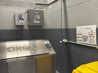 Garbage Doctor Duo and its scent tank on a block wall in a garbage room, above a food waste machine
