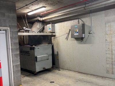 Garbage Doctor Duo on the wall of a basement waste room, beside the chute over a galvanised rubbish bin
