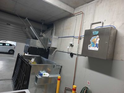 Garbage Doctor Ozone on a car park wall, beside a chute's hopper over a galvanised rubbish bin