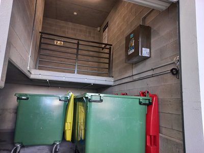 Garbage Doctor Ozone high on a bin room wall, above green 660-litre bins with yellow and red lids