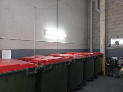 Garbage Doctor Ozone at the end of a long rubbish room lined with red-lidded bins