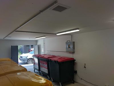 Garbage Doctor Ozone in a ground-floor bin store, above red-lidded waste bins by the roller door