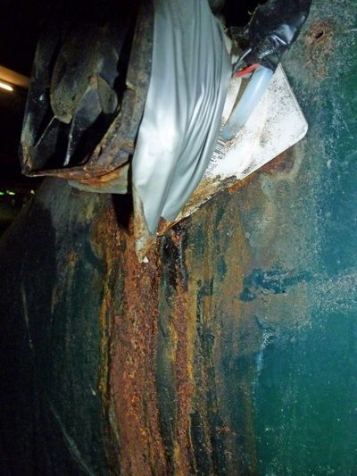 Rust running down a green steel garbage chute from where a spark-type ozone generator's taped hose goes in