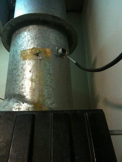 Rust streaks below a corona discharge generator's hose fitting on a round galvanised refuse chute, above a bin
