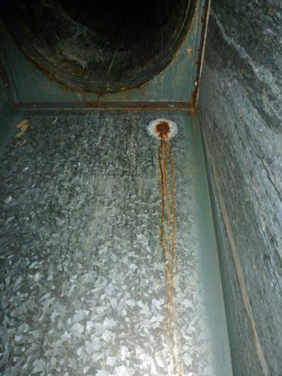 Inside a galvanised waste chute's discharge: rust spreading from the hole where a spark-type generator's hose went in