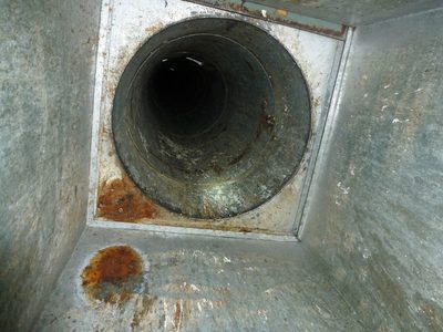 Looking up a garbage chute: rust eaten into the galvanised steel beside its round opening, from a spark-type generator