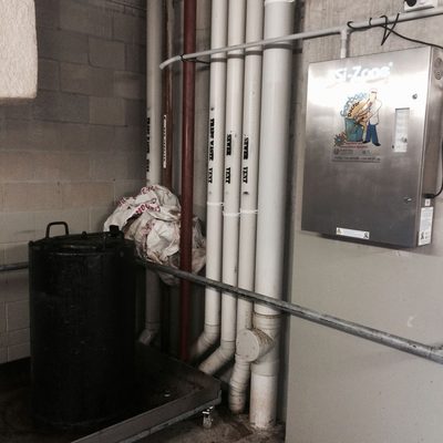 Garbage Doctor on the wall of a grease trap room, beside the trap's white vent pipes