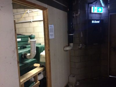 Garbage Doctor high on the wall of a grease trap room, above a green above-ground grease arrestor
