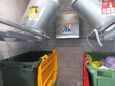 A Garbage Doctor on the wall between two chutes, above green and yellow bins