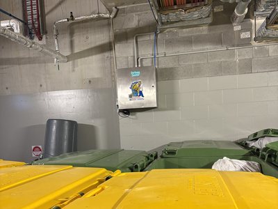 A Garbage Doctor Ozone on a block wall above yellow- and green-lidded bins