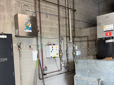 A Garbage Doctor Ozone on a compactor room wall, above its pipes and a galvanised bin