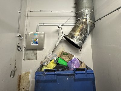 A Garbage Doctor Ozone beside a garbage chute's discharge, over a blue bin of rubbish