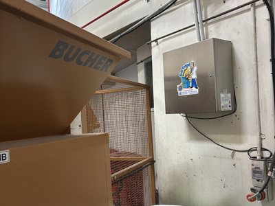 A Garbage Doctor Ozone HD on a bin room wall, beside a waste hopper above green bins